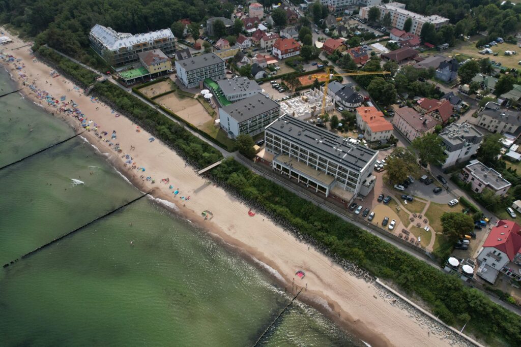 pexels-photo-13443583-13443583 Aerial shot capturing a town along a sandy beach by the ocean, featuring buildings and greenery.